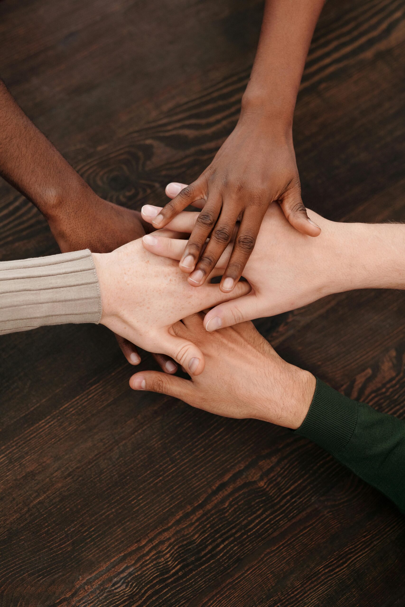 Home Close-up of diverse hands stacked together on wooden surface symbolizing teamwork and unity.