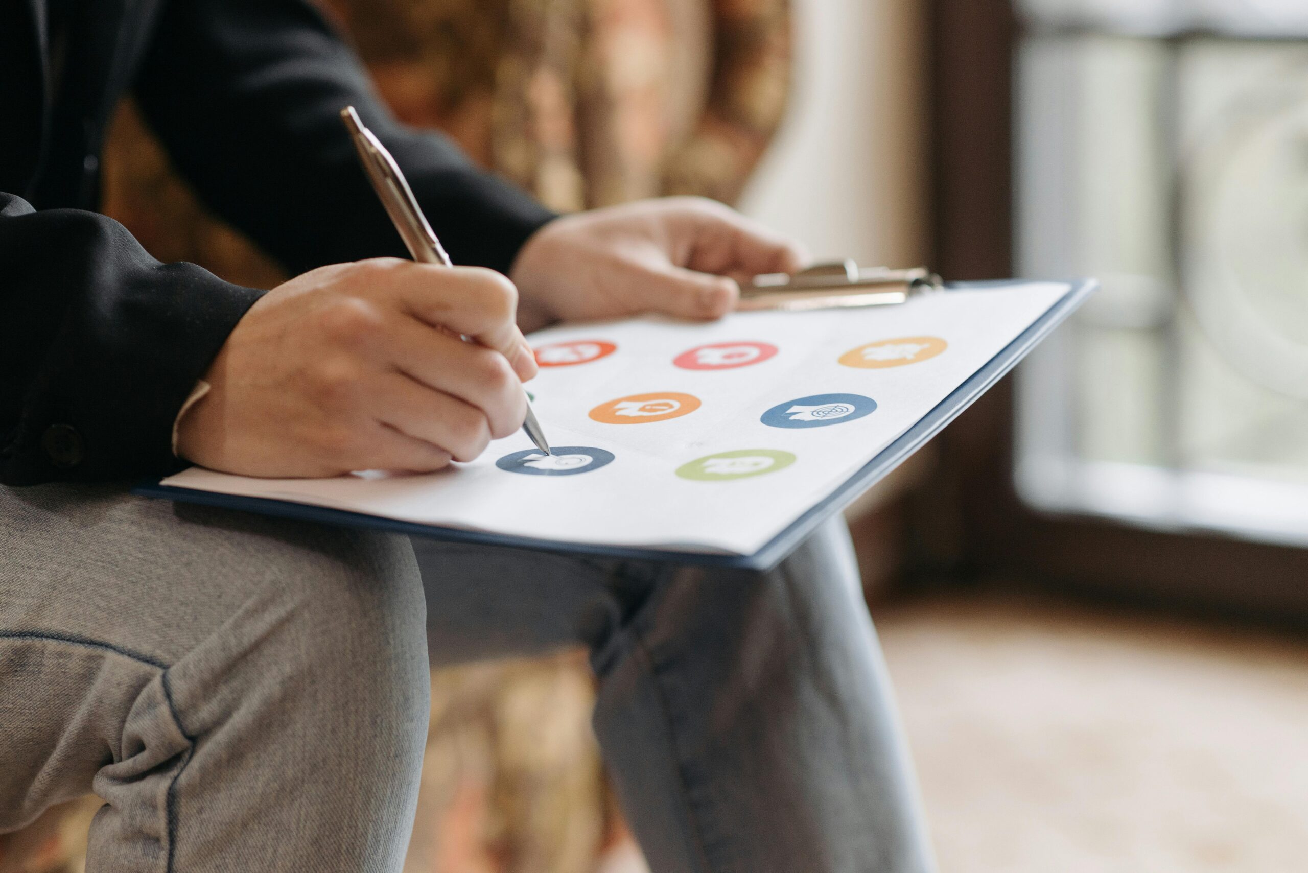 Home Close-up of a person writing on a clipboard with colorful icons.